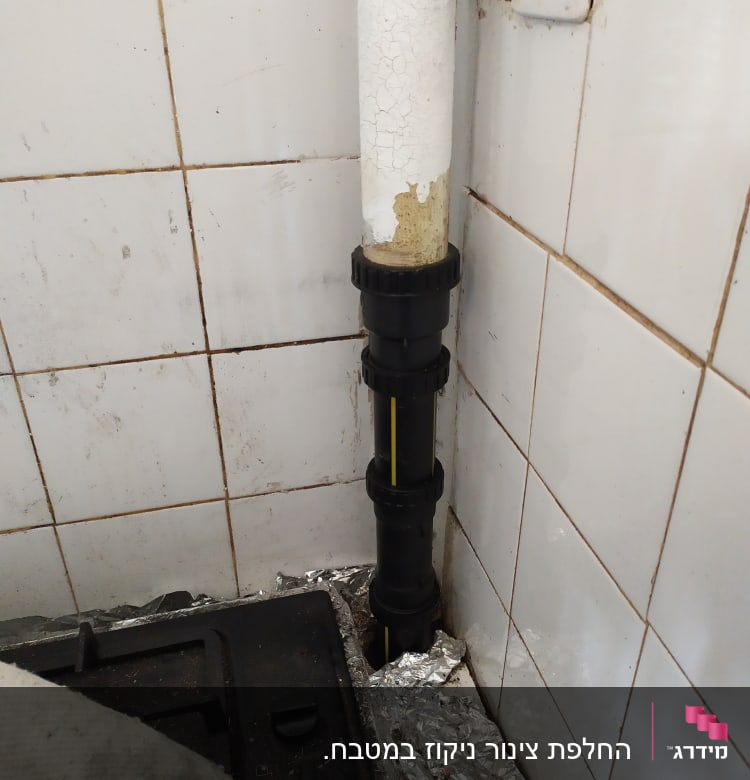 צינור פלסטיק שחור עם חיבורים ליד קיר אריחים